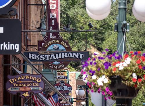 Colorful signs for various businesses, including a restaurant and tobacco shop, hang in a historic street setting.