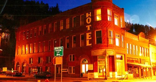 Historic brick hotel illuminated at night, with a municipal parking lot sign in front and trees in the background.