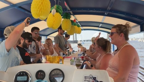 A lively group of people enjoying drinks on a boat, decorated with yellow pineapple decorations.