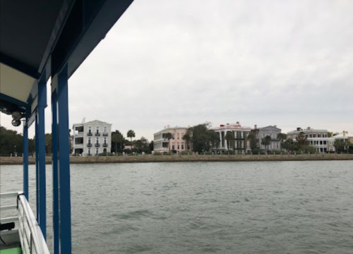 View of waterfront homes along a cloudy riverbank, seen from a boat.