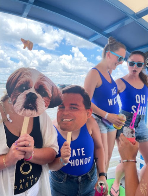 Group of friends on a boat wearing matching swimsuits, holding funny face masks and enjoying a sunny day.