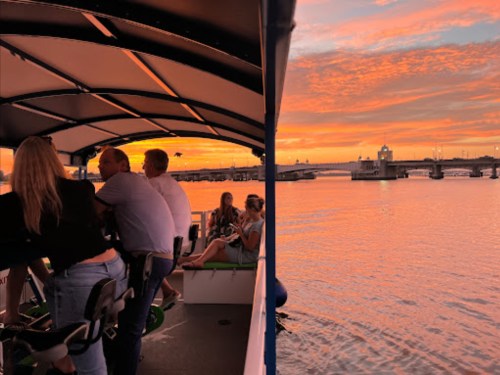People enjoying a boat ride at sunset, with vibrant orange and pink skies reflecting on the water.
