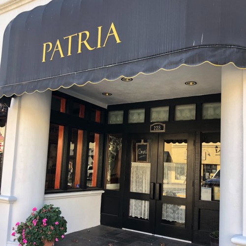 Exterior of a restaurant named "Patria," featuring a black awning and a welcoming entrance with potted flowers.