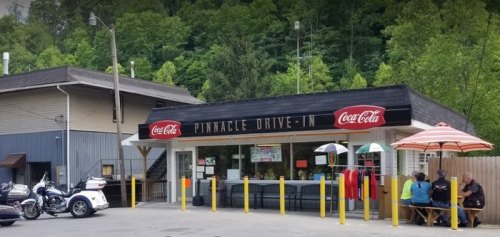A cozy drive-in restaurant with a Coca-Cola sign, outdoor seating, and lush greenery in the background.