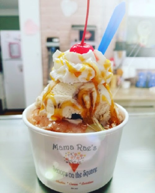 A delicious ice cream sundae topped with whipped cream, a cherry, and caramel sauce in a cup from Mama Rae's.