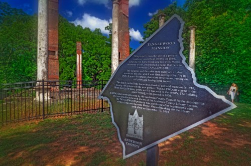 Sign marking Tanglewood Mansion ruins, with historical information and a map outline of Anderson County, surrounded by greenery.