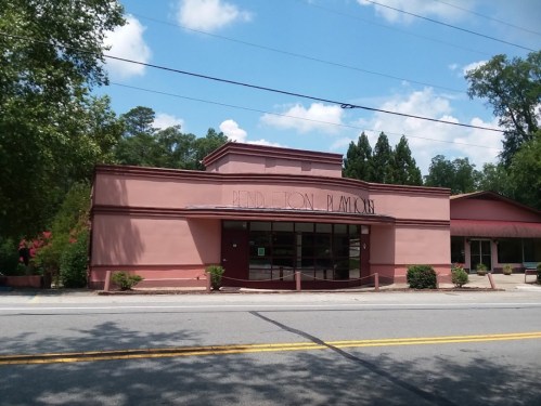 A pink building with "Mend-Ton Playhouse" sign, surrounded by trees and a clear blue sky.