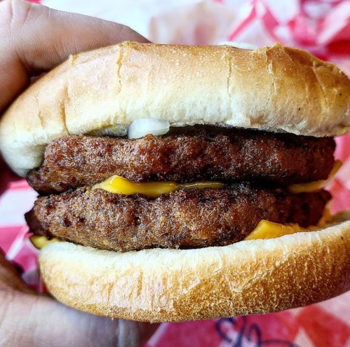 A hand holding a double cheeseburger with two beef patties and melted cheese, nestled in a soft bun.