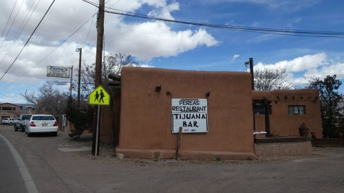 A rustic adobe building with a sign for "Perea's Restaurant Tijuana Bar" near a road with a pedestrian crossing sign.