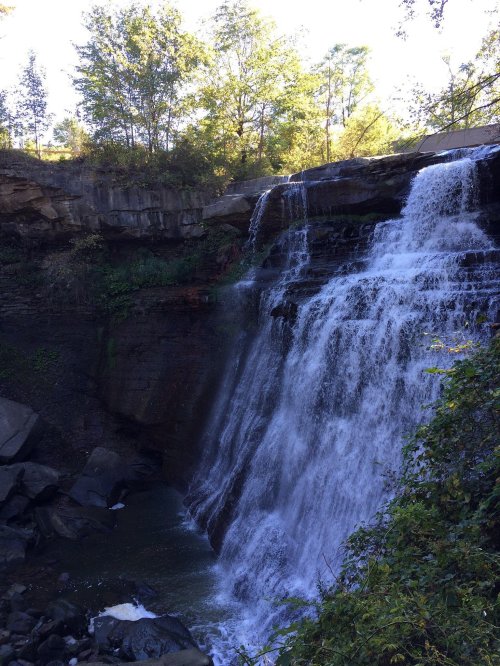 A cascading waterfall surrounded by lush greenery and rocky cliffs under a clear blue sky.