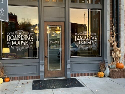 Exterior of a restaurant called "Boarding House," featuring large windows, a wooden door, and autumn decorations.
