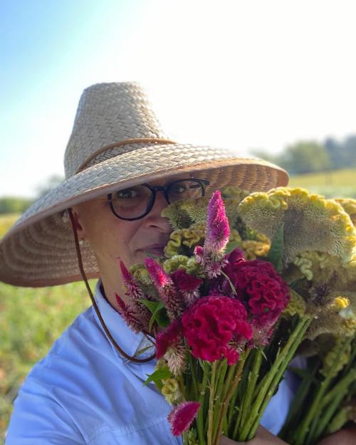 A person wearing a large straw hat holds a bouquet of colorful flowers in a sunny field.