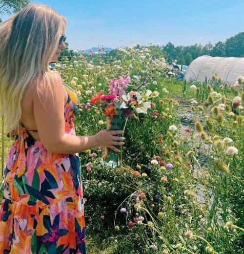 A woman in a colorful dress holds a bouquet of flowers in a vibrant field filled with blooming plants.