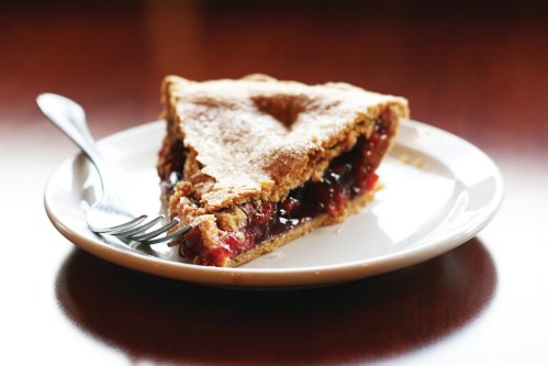 A slice of cherry pie on a white plate with a fork, showcasing a flaky crust and vibrant filling.