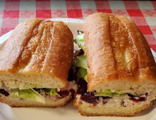 Two sandwich halves on a plate, filled with lettuce and a creamy spread, on a red and white checkered tablecloth.