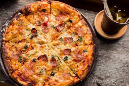 A freshly baked pizza topped with pepperoni, cheese, and vegetables, served on a wooden table with a drink.