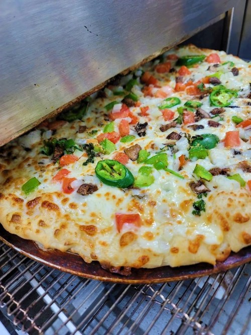 A freshly baked pizza with melted cheese, jalapeños, tomatoes, and green peppers, just out of the oven.