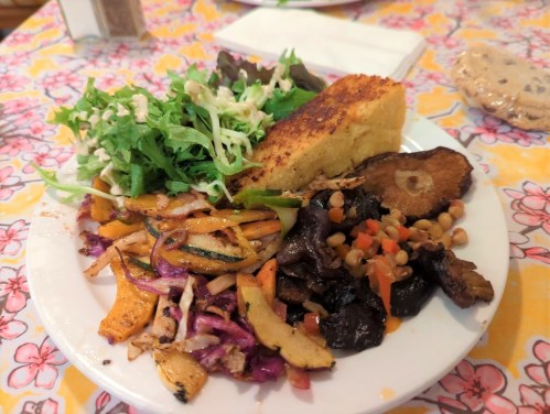 A plate of colorful vegetables, greens, cornbread, and a variety of beans, served on a floral tablecloth.
