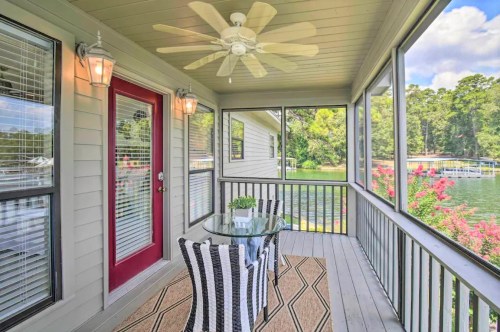 A screened porch with a glass table, striped chairs, and a view of a lake surrounded by trees.