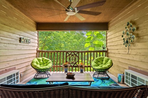 Cozy porch with green chairs, a table, and a view of lush greenery outside.
