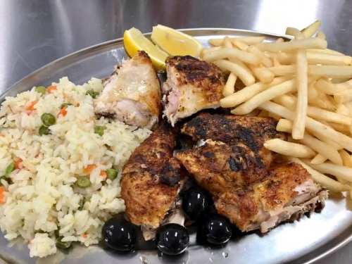 A plate of grilled chicken with rice, olives, French fries, and lemon wedges.