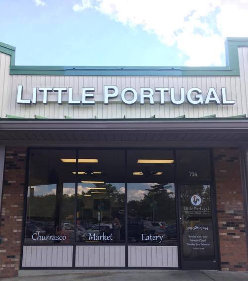 Sign for "Little Portugal" featuring a churrasco market and eatery, with large windows and a welcoming storefront.