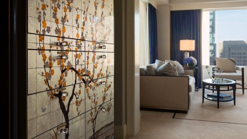 A stylish hotel room featuring a decorative wall with floral design, a cozy seating area, and large windows.