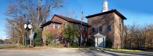 A brick building with a clock tower, flag, and landscaped area, representing a municipal or community center.