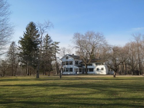 A white house surrounded by trees on a grassy lawn under a clear blue sky.