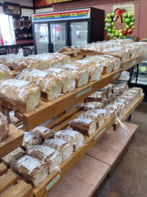 Loaves of bread neatly arranged on wooden shelves in a store, with a festive wreath in the background.