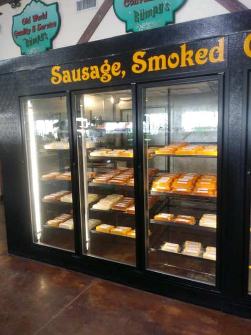 Display case filled with various types of smoked sausages and cheeses in a market setting.