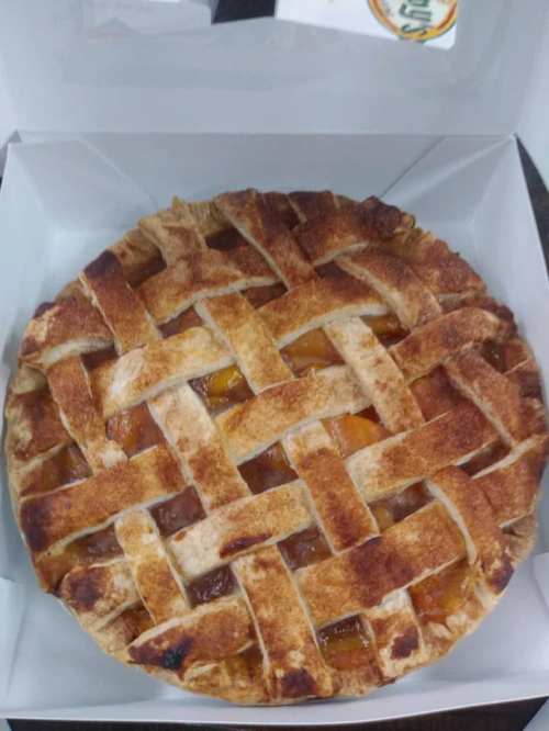 A freshly baked lattice-top pie in a white box, showcasing a golden-brown crust and visible fruit filling.