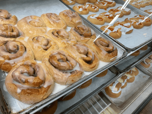 Freshly baked cinnamon rolls with icing, displayed on trays in a bakery.