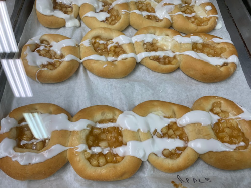 Freshly baked apple pastries drizzled with white icing on a parchment-lined tray.