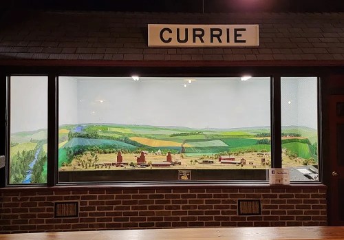 A display window featuring a miniature landscape with farms and rolling hills, labeled "CURRIE."