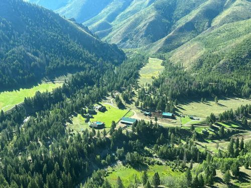 Aerial view of a lush valley surrounded by mountains, featuring scattered cabins and dense forests.