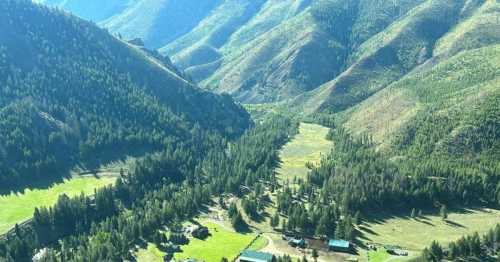 Aerial view of a lush green valley surrounded by mountains, with scattered buildings and trees in the foreground.