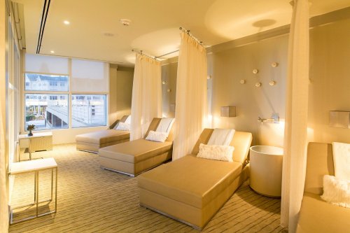 A serene spa room with lounge chairs, soft lighting, and sheer curtains, creating a relaxing atmosphere.