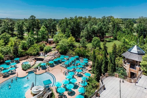 Aerial view of a resort pool area with turquoise umbrellas, surrounded by lush greenery and a waterslide.