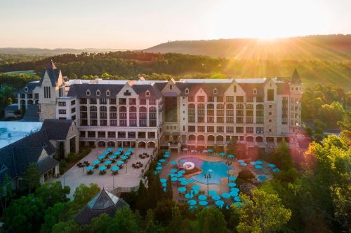 Aerial view of a luxurious hotel with a pool and lounge chairs, surrounded by trees and mountains at sunset.