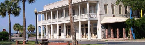 Historic building with a porch, palm trees, and a clear blue sky in the background.