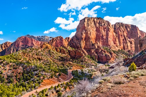 A scenic view of red rock formations and green vegetation under a blue sky with scattered clouds.