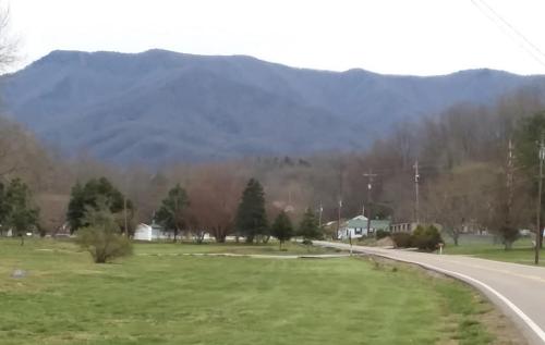 A scenic view of rolling mountains in the background, with a winding road and green fields in the foreground.