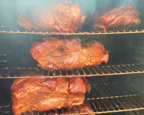 Smoked meats on racks inside a smoker, showcasing a rich, dark brown exterior.
