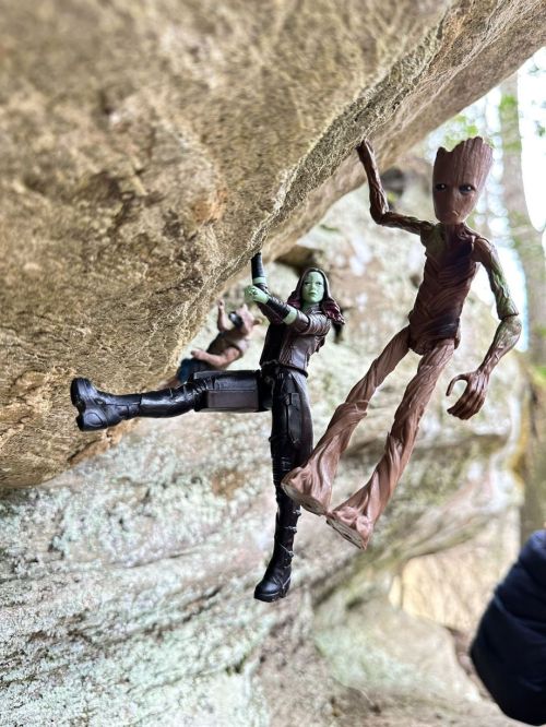 Two action figures, one green and one brown, are posed climbing a rocky surface in a natural setting.