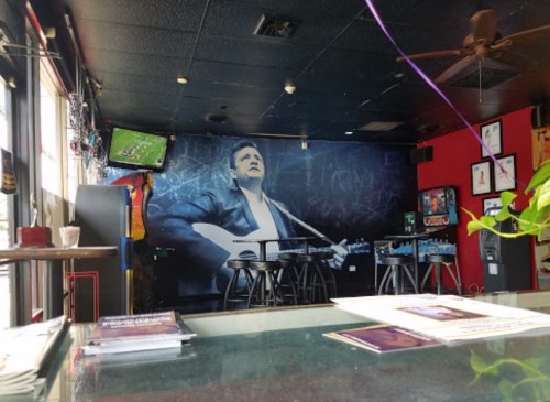 Interior of a bar featuring a mural of a musician, with tables, pinball machines, and a TV in the background.