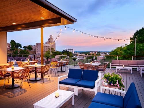 Rooftop terrace with seating, string lights, and a sunset view over a city skyline.