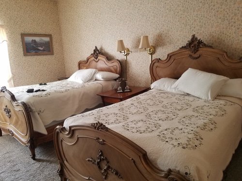 A cozy bedroom with two vintage wooden beds, floral wallpaper, and soft lighting from bedside lamps.