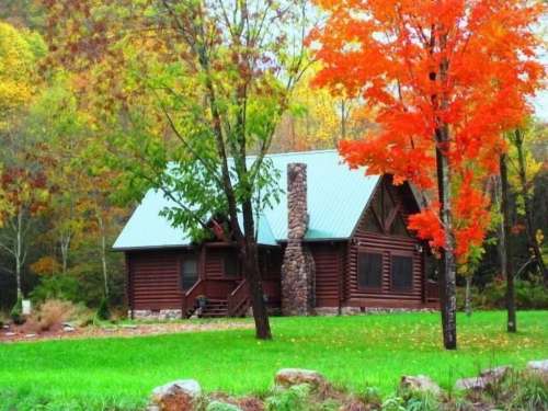 A cozy log cabin surrounded by vibrant autumn trees and lush green grass.