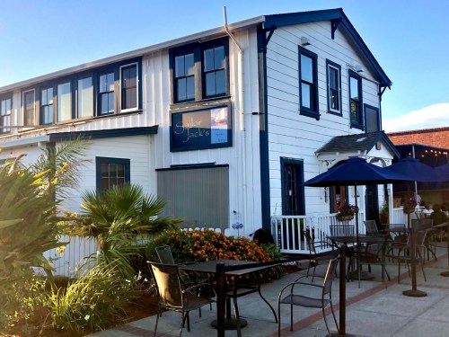 A white building with blue trim, featuring a sign for "Sailor Jack's," surrounded by flowers and outdoor seating.